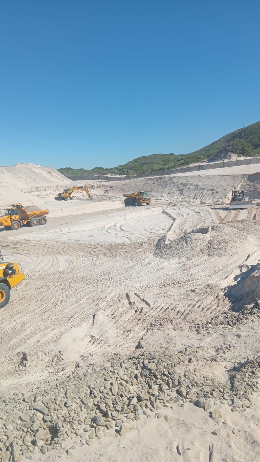 Excavators and articulated dump trucks shaping a bulk earthworks platform