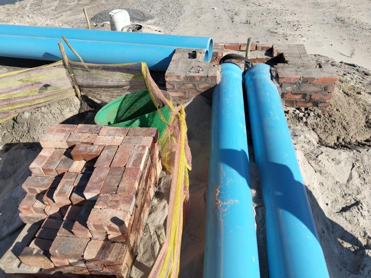 Large-diameter blue PVC pipes laid in a trench beside stacked clay bricks