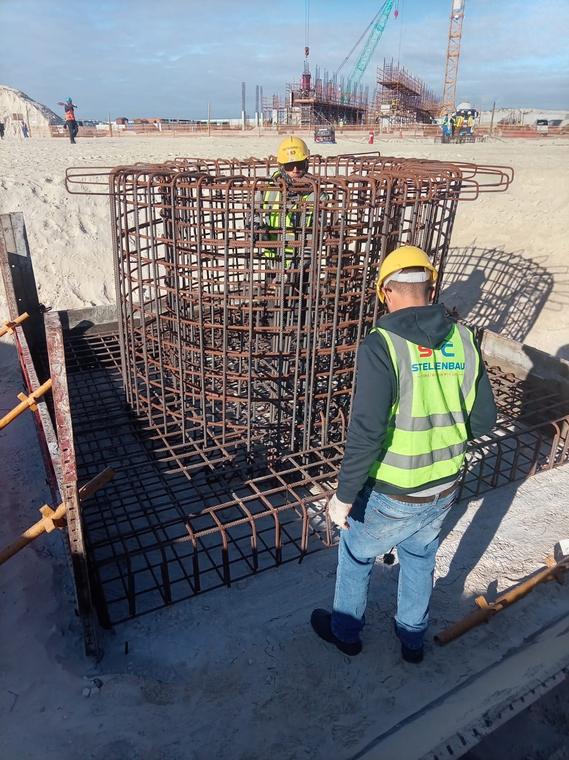 Workers positioning a circular steel reinforcement cage inside shuttered formwork