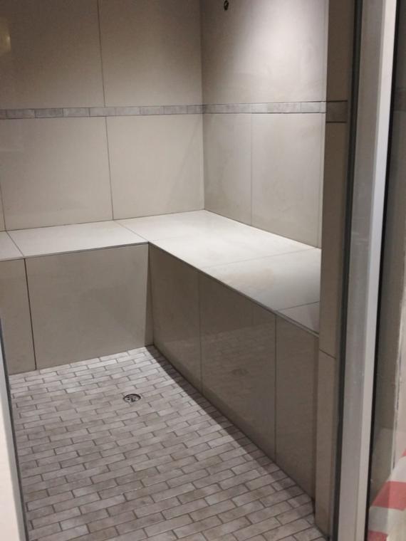 Shower with a tiled corner bench and brick-bond floor tiling to the drain