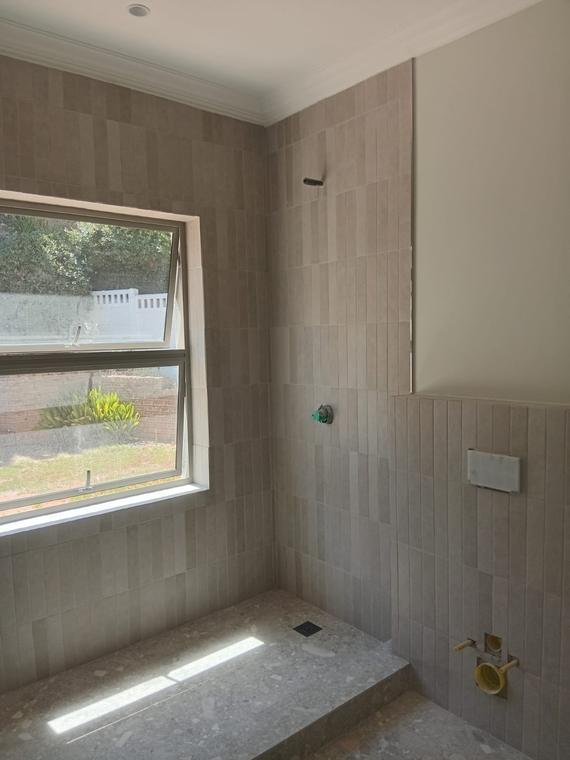 Shower tiled in vertical stack-bond tiles with a terrazzo floor and threshold