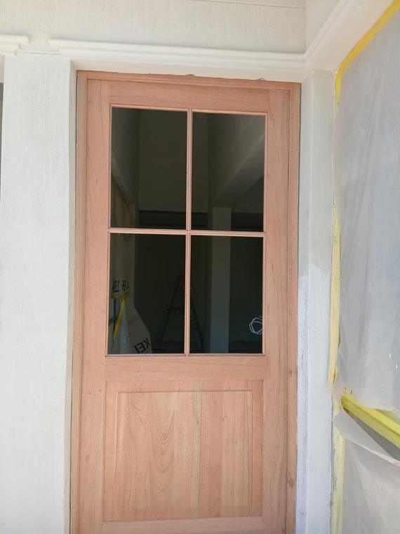 Hardwood four-pane door hung in a painted frame with cornice above