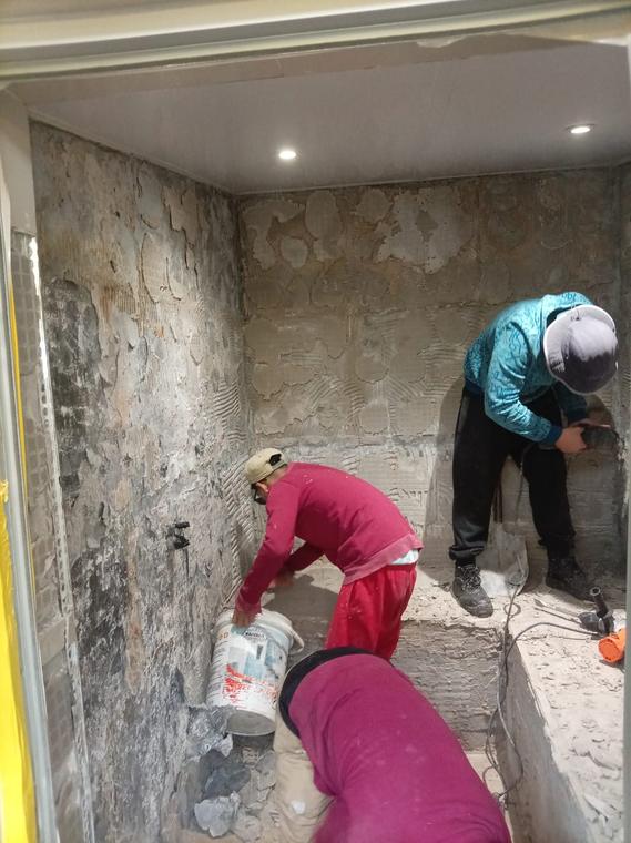 Two workers chipping off old tiles and preparing walls for re-tiling