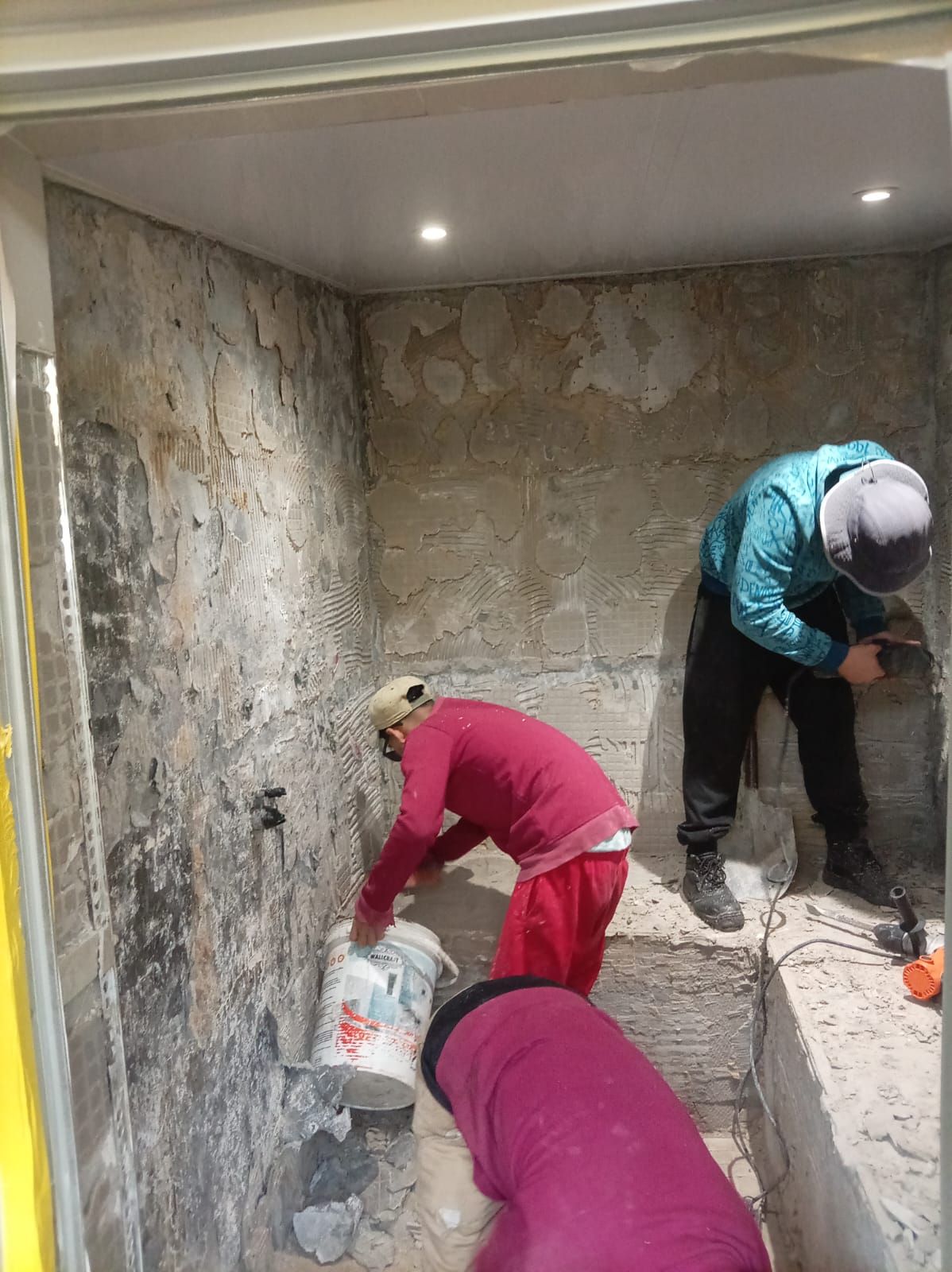 Two workers stripping old tiles and preparing walls in a bathroom refurbishment